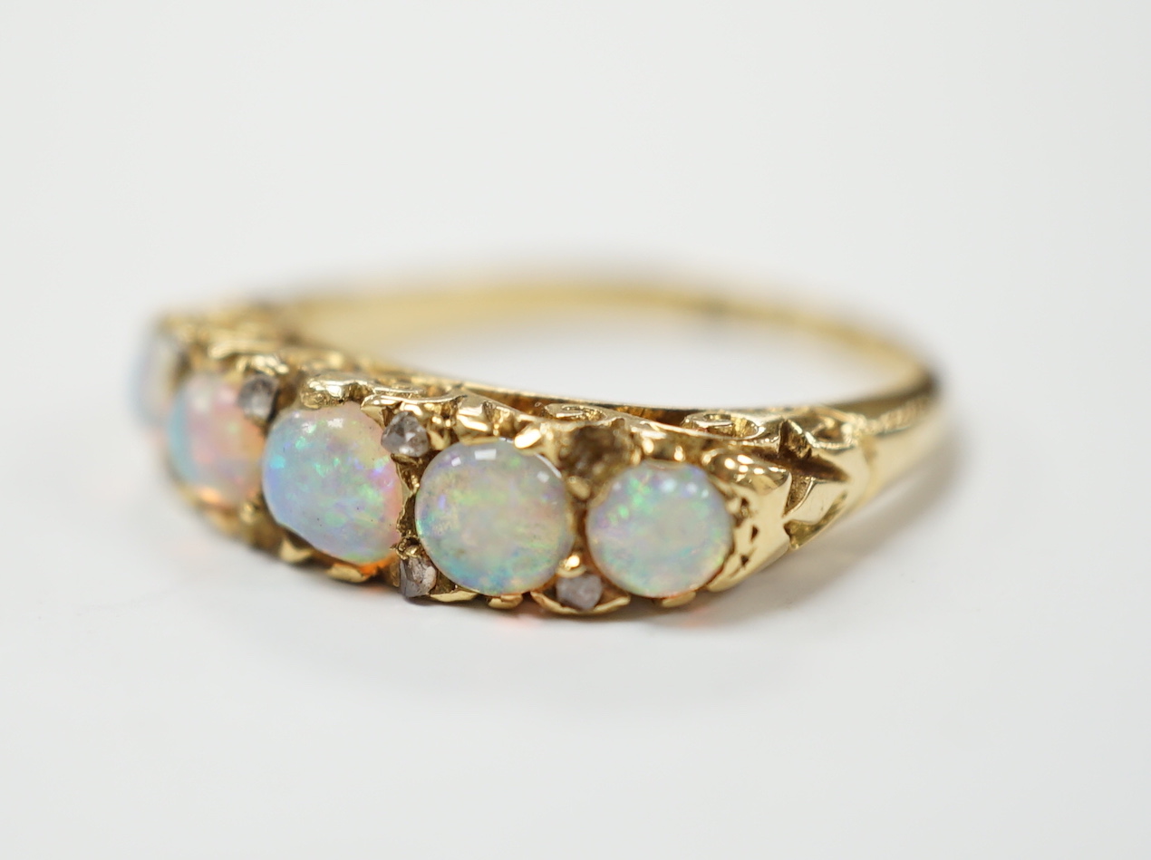 A late Victorian yellow metal and white opal five stone ring with diamond chip set spacers, size M